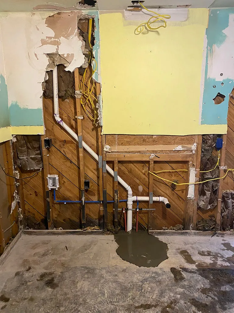 Opened wall showing new drain and water lines during a renovation