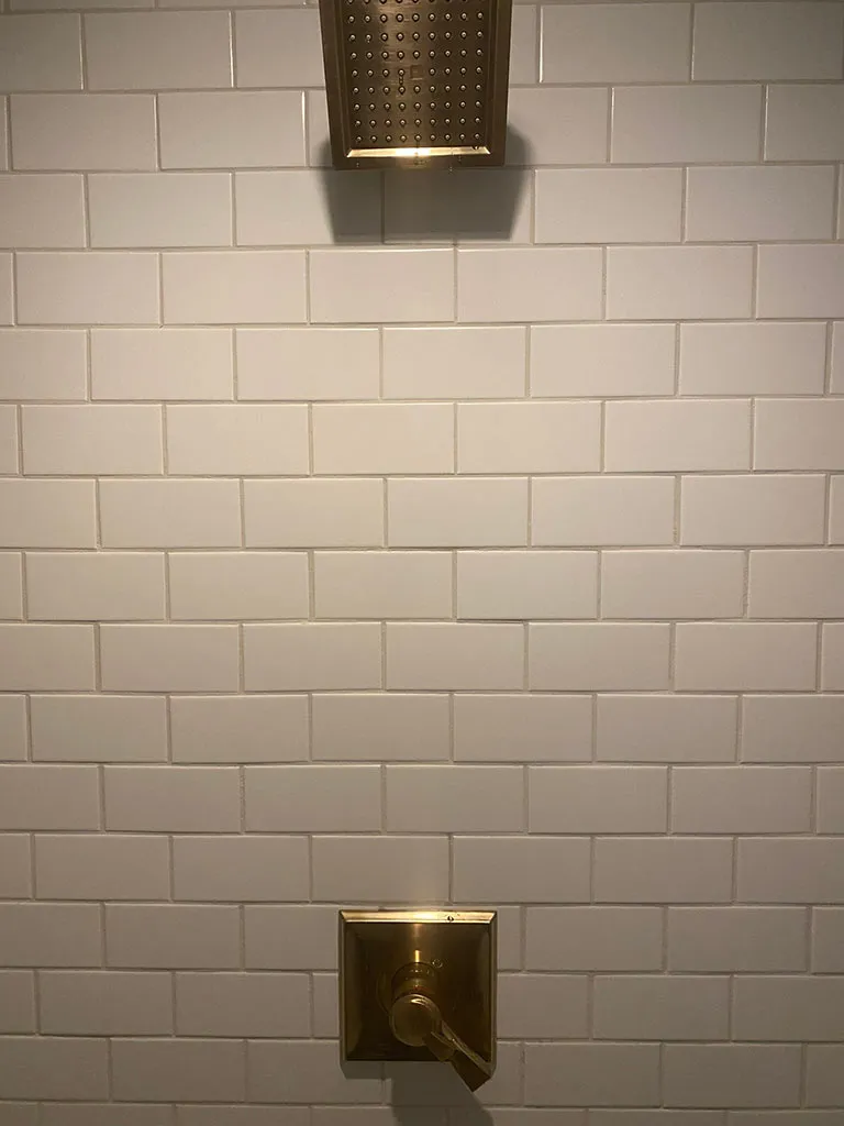 Finished subway tile shower with a brass rain head and valve