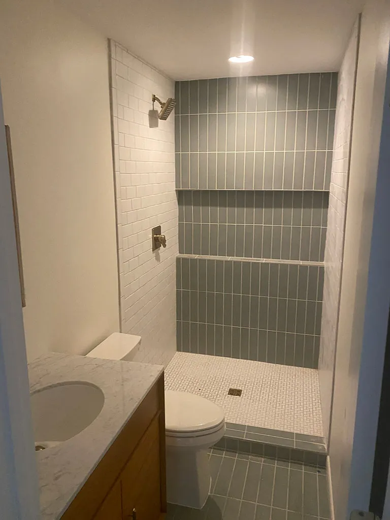 Finished walk-in shower with gray tile, a new toilet, and a vanity